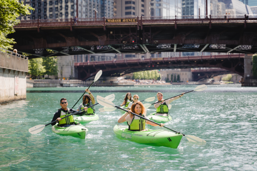 Group of friends in green kayaks traverse down the Chicago River on a nice spring day